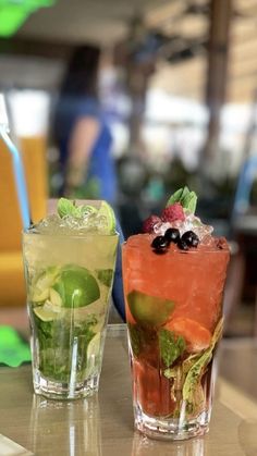 two glasses filled with drinks sitting on top of a table next to each other,