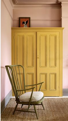 a yellow armoire sitting next to a white chair in a room with pink walls