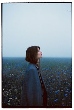 a woman standing in a field looking up into the sky with flowers all around her