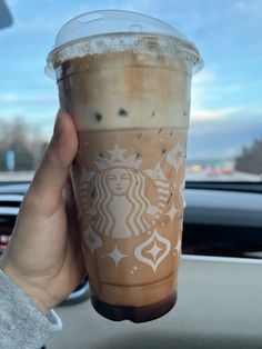 a person holding up a cup of coffee in their hand while sitting in a car