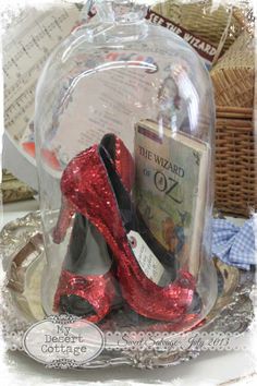 red high heeled shoes under a glass dome on a tray with books in it