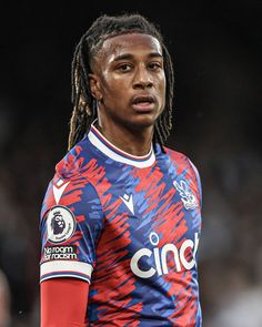 a man with dreadlocks standing in front of a crowd wearing a blue and red shirt