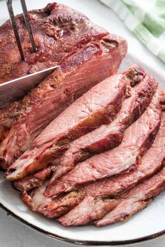 sliced meat on a plate with a knife and fork sticking out of the top one