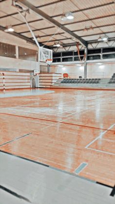 an empty gym with hard wood flooring and basketball hoop in the center, surrounded by bleachers