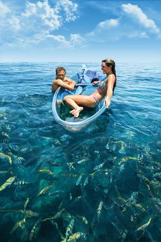 two people on a boat in the ocean with fish around them and blue sky above