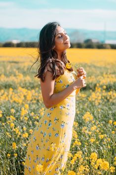 a woman in a yellow dress standing in a field of flowers looking up at the sky