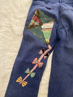 a pair of blue jeans with an embroidered kite on the back and side, sitting on top of a white sheet