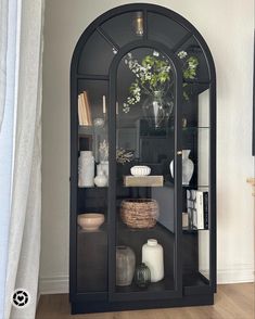 a glass display case with plants and vases on it in the corner of a room