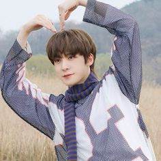 a young man standing in a field holding his hands up to his head with one hand