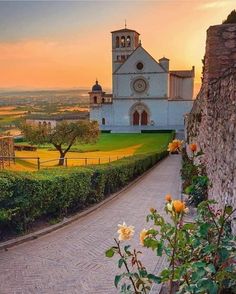 the sun is setting over an old church with roses growing on the sidewalk in front of it