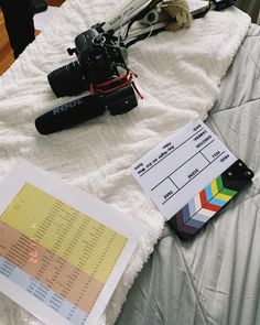 a camera and some other items on a white bed sheet with a book next to it