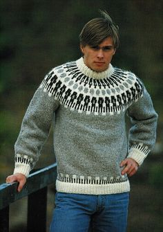 a man wearing a sweater and jeans standing next to a fence with his hands on his hips