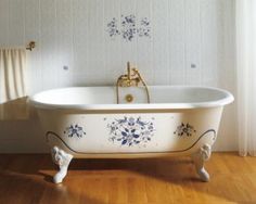 an old fashioned bathtub with blue flowers painted on the side and gold faucet