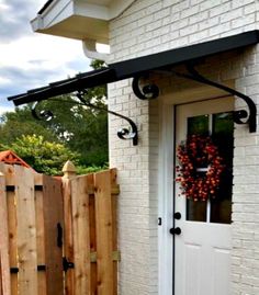 a white door with a black awning next to a brick wall and wooden fence