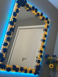 a blue and yellow flowered mirror on the wall next to a vase with flowers