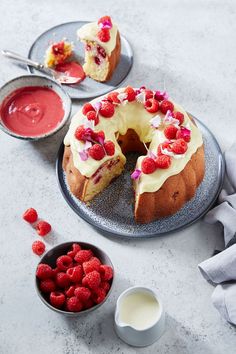 a cake with white frosting and raspberries next to two bowls of fruit