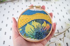 a hand is holding a small embroidery art piece