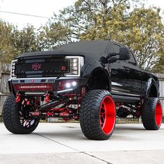 a black truck with red rims parked in front of a fence