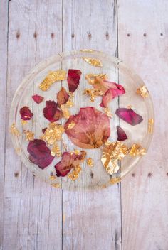 a glass plate filled with gold flakes on top of a wooden table next to a red rose