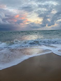 the ocean waves come in to shore as the sun is setting over the water and clouds