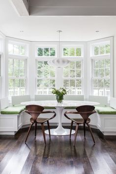 a dining room table with two chairs and a bench in front of the bay window