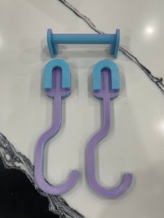 two blue and purple hooks hang from a marble counter top, with one hook attached to the wall