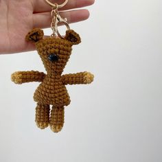 a small crocheted teddy bear keychain being held by someone's hand