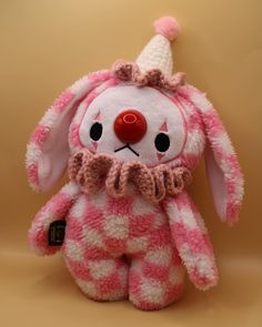 a pink and white stuffed animal with a clown hat on it's head, sitting against a beige background