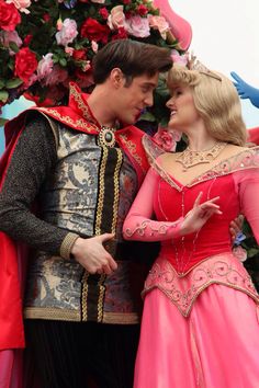 a man and woman dressed in costumes standing next to each other with flowers behind them