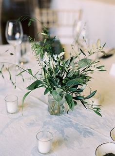 the table is set with white linens, silverware and flowers in glass vases