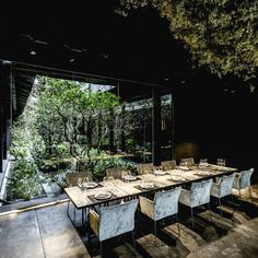 a long table with white chairs and plates on it in front of a glass wall