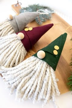 three christmas trees made out of yarn sitting on top of a wooden board next to pine cones