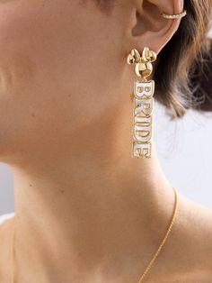 a woman wearing gold earrings with the word bride engraved on it's back side