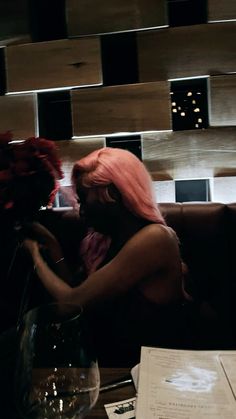 a woman with pink hair sitting at a table next to a vase filled with flowers