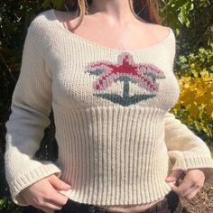 a woman standing in front of some flowers wearing a sweater with an anchor on it