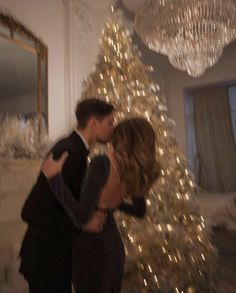 a man and woman are kissing in front of a christmas tree with lights on it