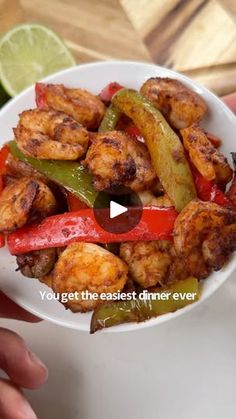 a person holding a white bowl filled with chicken and peppers next to a lime wedge