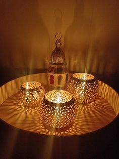 four candles are lit on a tray with a lantern in the middle and shadows cast across it