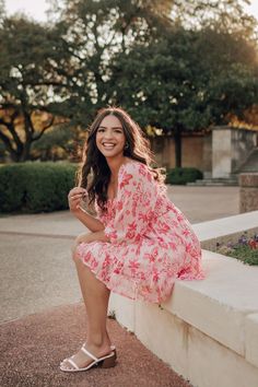 a woman in a pink dress is sitting on a ledge and smiling at the camera