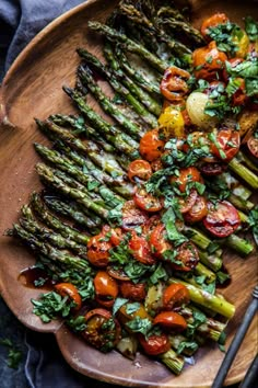 asparagus, tomatoes and other vegetables on a wooden platter with a fork