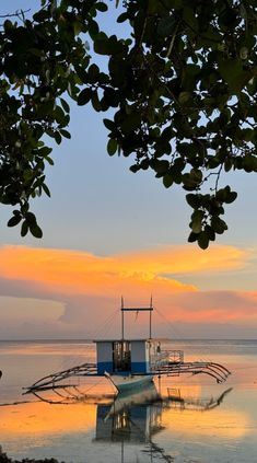 a boat sitting on top of a body of water under a cloudy blue and orange sky