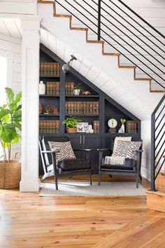 a living room with two chairs and a book shelf under the stair case in front of it