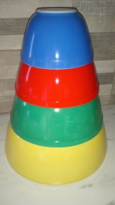 a stack of colorful plastic bowls sitting on top of a white counter next to a wooden wall