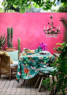 an outdoor dining area with cactus and potted plants on the table, pink wall in background