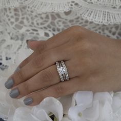 a woman's hand with two wedding rings on her finger and flowers in the background