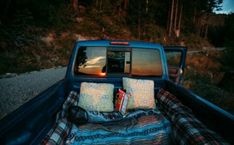 the back end of a pick up truck with pillows and blankets in the bed