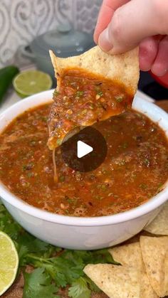 someone dipping tortilla chips into a bowl of chili