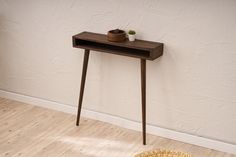 a small wooden table with a plant on it in front of a white painted wall