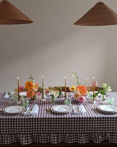 the table is set with plates and flowers on it, along with two hanging lamps