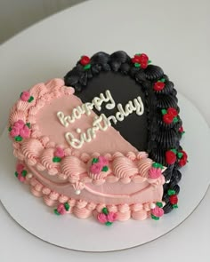 a heart shaped birthday cake with pink frosting and black icing, on a white plate